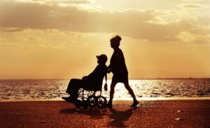 resident in wheelchair with carer on beach