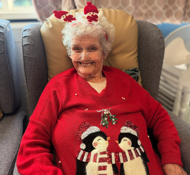 resident with a penguin christmas jumping smiling in a chair